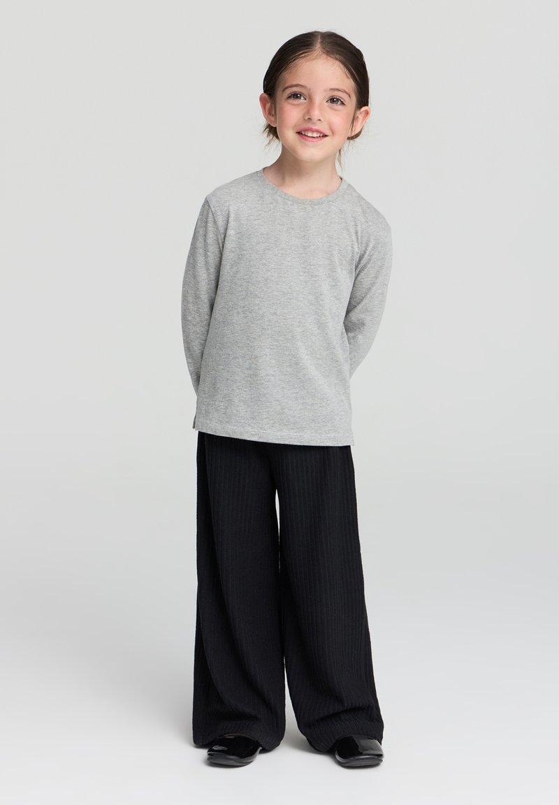 Maglietta a maniche lunghe grigia abbinata a pantaloni neri a gamba larga e a coste, caratterizzati da una vestibilità rilassata e un design minimalista. Scarpe nere slip-on.