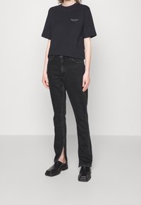 Black cotton t-shirt with short sleeves, paired with high-waisted black jeans featuring side slits at the ankles, and black footwear.