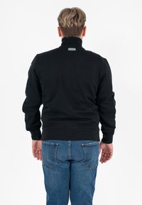 Zwarte sweatshirt met ritssluiting in de hals, met een geribde kraag, snugger aansluitende mouwen en elastische tailleband, gecombineerd met blauwe denim jeans. Effen textiel zonder zichtbare patronen.