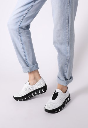Witte instapschoenen met een geperforeerd patroon, zwarte dikke zool met witte chevronaccenten en elastische zijkanten voor comfort.