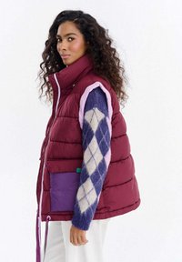 Pikowana, bezrękawnik w kolorze bordowym z jasnoróżowymi akcentami. Posiada fioletową kieszeń naszywaną i sznurki ściągające u dołu. Teksturowany i pikowany wzór.