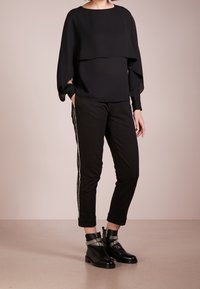 Blusa nera a strati con maniche ampie, abbinata a pantaloni neri con una striscia laterale argentata e stivaletti con accenti metallici.