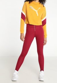 Żółta krótka bluza z logo, czerwone legginsy i białe sneakersy. Cechy to blokowanie kolorów oraz zamek b�łyskawiczny na spodniach.