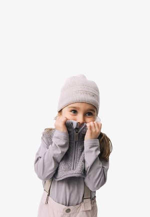 Grauer Fleece-Pullover mit Reißverschluss, über einem Langarmshirt getragen. Hellrosa Hosenträger und eine gestrickte, hellgraue Mütze.
