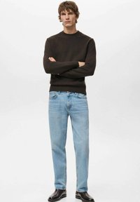 Donkerbruin gebreide trui met ronde hals, gecombineerd met lichtblauwe denim jeans met rechte pijpen. Glanzende zwarte enkellaarzen maken de look compleet.