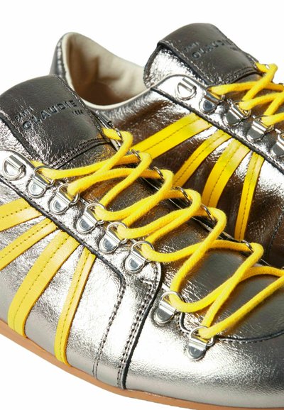 Sneaker metallici argentati con lacci e strisce gialle. Presentano occhielli con dettagli metallici. Tessuto liscio, punta arrotondata e suola in gomma.