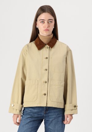 Giacca di tela beige con colletto in velluto a coste marrone, dotata di chiusura frontale con bottoni, due tasche laterali e polsini con regolazione a scatto.