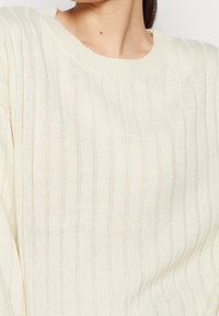 Maglione lavorato a maglia color crema con texture a coste verticali, ampio collo girocollo e vestibilità morbida.