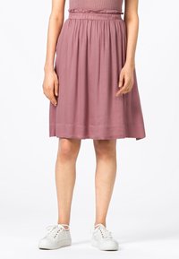 Zmačkaný pas, sukně do kolen v látce v jemné růžové barvě; lehká, měkká textura; v kombinaci s bílými teniskami pro ležérní vzhled.