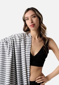 Manta de rayas grises y blancas sobre el hombro, con una textura suave y un diseño recogido, contrastando con una blusa negra.