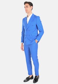 Completo blu doppiopetto realizzato in tessuto texturizzato, con revers a punta e mocassini neri. Pantaloni slim-fit con taglio su misura.