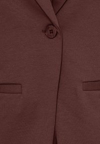 Gros plan d'un blazer marron avec un bouton fermé et deux poches fendues horizontales de chaque côté.