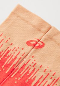 Calcetines de color durazno con una superficie texturizada, que presentan un diseño degradado que transiciona a rojo en la parte inferior y un pequeño logo cerca de la parte superior.