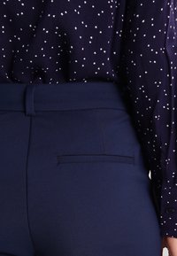 Granatowe spódnice z wysokim stanem o gładkim wykończeniu, z tylnią kieszenią, zestawione z ciemną bluzką w gwiazdy.