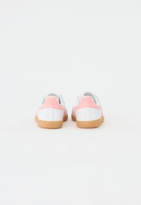 Witte sneakers met roze accenten, gestructureerde panelen en een gumrubberen zool. Achteraanzicht toont een gevoerde hiel en contrasterende stiksels.