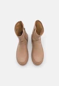 Botas de tobillo de cuero beige con cremallera lateral, punta redondeada y suela texturizada. Interior forrado con un suave material marrón claro, acabado liso.