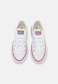 Zapatillas de lona blancas con detalles rojos, con un diseño de corte bajo, puntera redonda y cierre de cordones clásico. Marca Converse All Star visible.