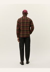 Camisa de cuadros en tonos burdeos, amarillo y verde, con un corte relajado. Combinada con pantalones oscuros y ajustados y zapatos marrones. Gorra en color a juego.