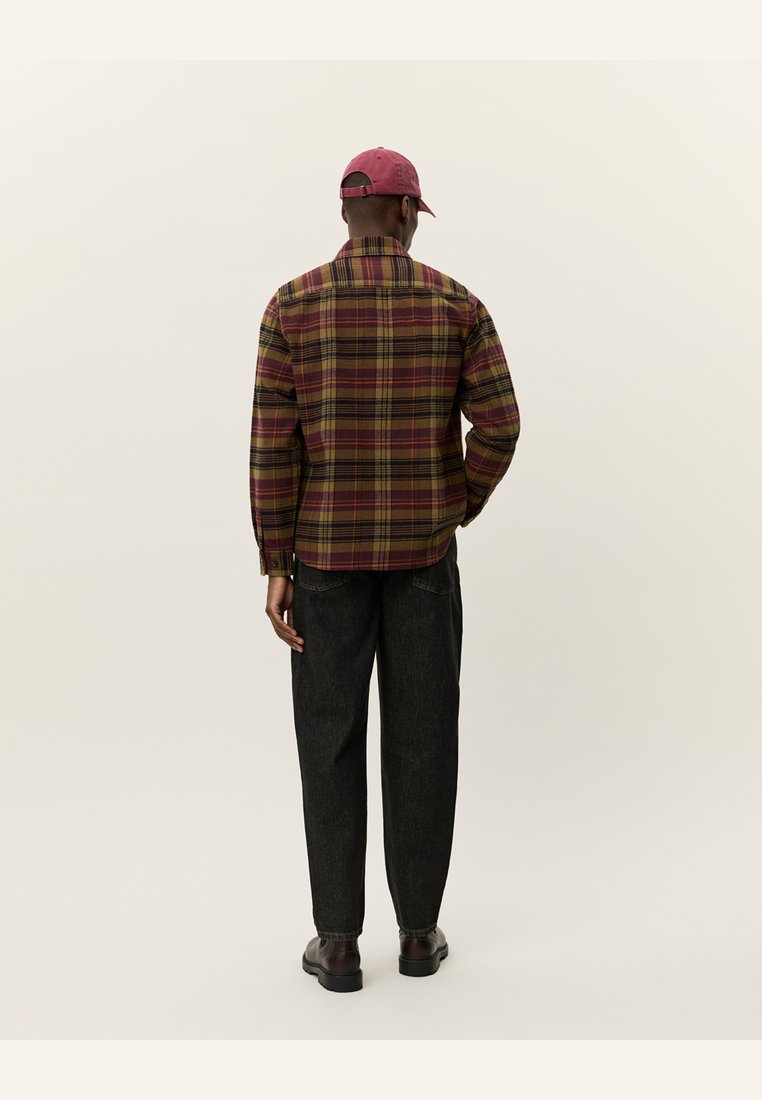 Camisa de cuadros en tonos burdeos, amarillo y verde, con un corte relajado. Combinada con pantalones oscuros y ajustados y zapatos marrones. Gorra en color a juego.