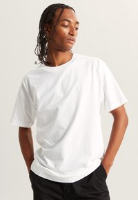 White crew-neck t-shirt with short sleeves, made from soft cotton. The fabric is smooth, with a relaxed fit and minimal design details.