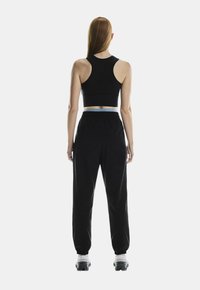 Soutien-gorge noir à dos nageur associé à un pantalon noir ample avec une taille élastique et une accentuation bleu pâle.
