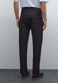 Mörka denimjeans med rak benleende, två bakfickor, diskret sömnad och en svart märkesskylt på midjebandet. Bärs med mörka skor.