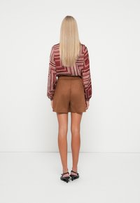 Brune semsket shorts med en avslappet passform, kombinert med en langermet bluse med multikolor geometrisk mønster. Modellen vises fra baksiden.