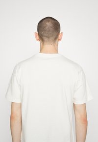 Bílé bavlněné tričko s kruhovým výstřihem, krátkými rukávy a uvolněným střihem. Zobrazeno ze zadní strany, odhalující jednoduchý design.