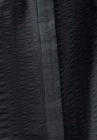 Tessuto nero con texture, caratterizzato da motivi a righe verticali e orizzontali; presenta una cerniera liscia lungo un lato. Materiale morbido e leggermente elasticizzato.
