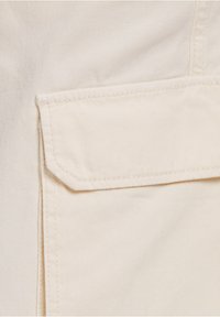 Beige bomullstyg med en strukturerad väv, med en fyrkantig ficka med rak överkant och rena sömdetaljer.