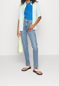 Camiseta de manga corta teñida en azul pastel y verde, top de tirantes azul acanalado, jeans de tiro alto en azul claro y chanclas blancas. Bolsa verde.