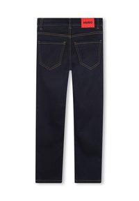 Jeans de mezclilla azul oscuro con una etiqueta roja en la parte trasera, diseño estándar de cinco bolsillos y detalles de costura amarilla en contraste.