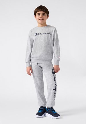 Gray cotton sweatshirt and sweatpants set with "Champion" logo in dark blue. Includes ribbed cuffs and relaxed-fit design. Navy sneakers.