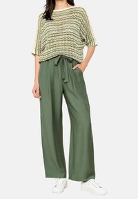 Stickad kortärmad topp med gröna och krämfärgade ränder, kombinerad med lätta olivgröna vida byxor och vita sneakers.