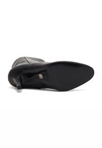 Botte de cheville en cuir noir avec un bout pointu, un talon fin et une finition lisse. Présente un design minimaliste avec une silhouette élégante.