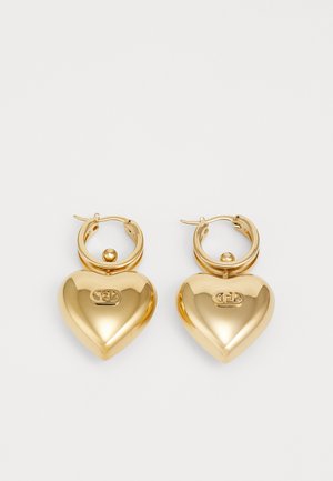 Gold-tone hoop earrings featuring a large heart-shaped pendant with a shiny surface and engraved logo detail.
