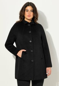 Cappotto nero di lunghezza media realizzato in tessuto strutturato con colletto alto, chiusura frontale con bottoni e tasche laterali. Finitura liscia e design minimalista.