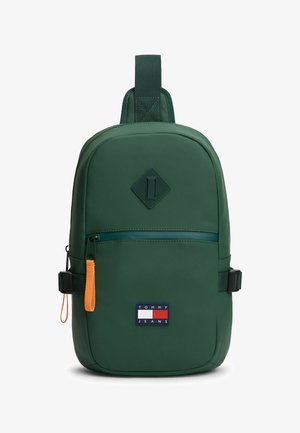 Dunkelgrüner Sling-Rucksack von Tommy Jeans mit vorderer Reißverschlusstasche, orangefarbenem Reißverschlusszug, verstellbaren Seitenträgern und diamantförmigem Detail.