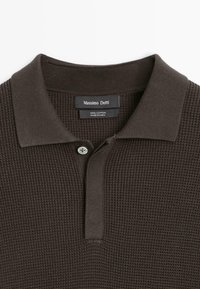 Polo in cotone marrone caratterizzata da un design a maglia waffle testurizzata, scollo con collo e chiusura con un solo bottone. Include etichetta Massimo Dutti.