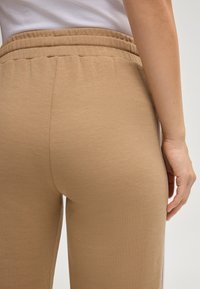 Hellbraune Baumwoll-Sweatpants mit elastischem Bund und Seitenstreifen, die eine glatte Textur und eine figurbetonte Passform bieten.