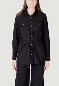 Camicia nera con bottoni a maniche lunghe, dotata di due tasche sul petto e coulisse regolabile in vita. Realizzata in un tessuto leggero e morbido.