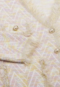 Cardigan pastel cu un model în zigzag în nuanțe de roz, galben și alb. Prezintă nasturi asemănători perlelor și franjuri texturate pe margini.