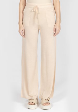 Beżowe spodnie o szerokich nogawkach z przednimi kieszeniami i sznurkiem w talii, noszone z kremowymi sandałami na platformie.