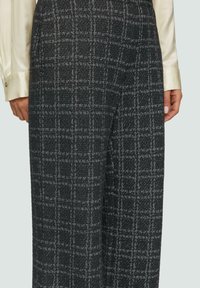 Zwart-wit geblokte broek van een gestructureerde stof, met een wijde pijpdesign en een zijzak. Draagt met een lichtgekleurde longsleeve top.