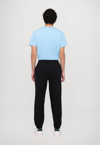 Light blue cotton t-shirt with short sleeves, paired with black sweatpants featuring elastic cuffs and a drawstring waist, worn with white sneakers.
