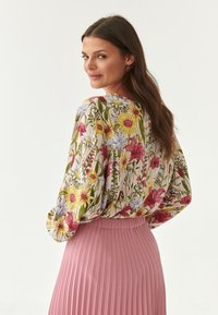 Blusa floral de manga larga con una variedad de colores sobre un fondo claro. Combinada con una falda rosa plisada. Textura de tela suave.