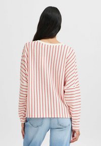 Pull rayé avec des motifs verticaux rouges et blancs. Matière tricot douce, coupe décontractée, manches larges et col arrondi. Associé à un jean en denim clair.