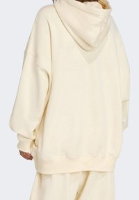 Sudadera de gran tamaño en color crema con capucha ajustable, mangas anchas y dobladillo acanalado. Textura suave con un detalle de costura mínimo.