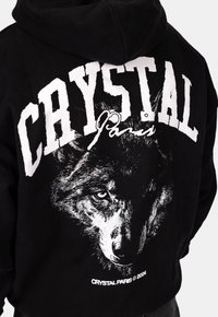 Felpa nera con cappuccio caratterizzata da grandi scritte bianche "CRYSTAL Paris" e un grafico dettagliato di un lupo sul retro. Tessuto morbido con vestibilità rilassata.