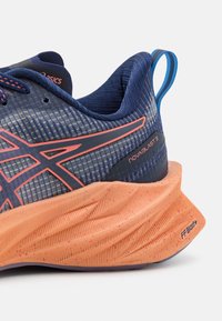 Gros plan du talon d'une chaussure de running bleue et orange avec semelle texturée, languette de tirage et marquage « NOVA BLAST 3 » et « FF BLAST+ ».